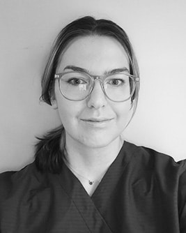 Svartvitt porträtt av en leende tandhygienist med uppsatt hår och glasögon mot en ljus bakgrund.