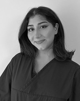 Svartvitt porträtt av en tandhygienist med långt mörkt hår. Personen bär en mörk tröja och tittar mot kameran mot en ljus, neutral bakgrund.