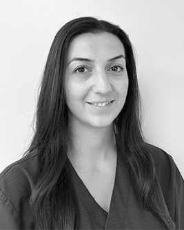 Svartvitt porträtt av en tandhygienist med långt mörkt hår. Personen bär en mörk tröja och tittar mot kameran mot en ljus, neutral bakgrund.